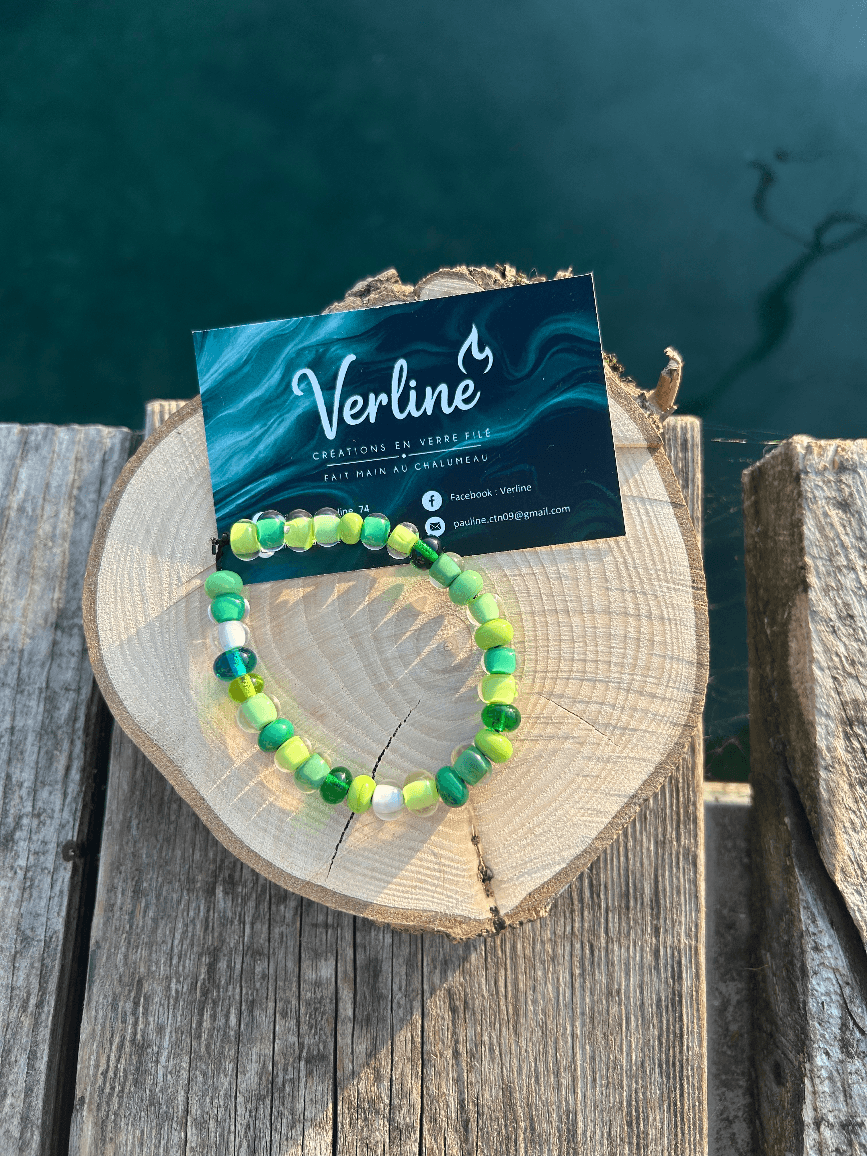 Bracelet de perles rondes aux nuances de vert et perles transparentes posé sur une tranche de bois.