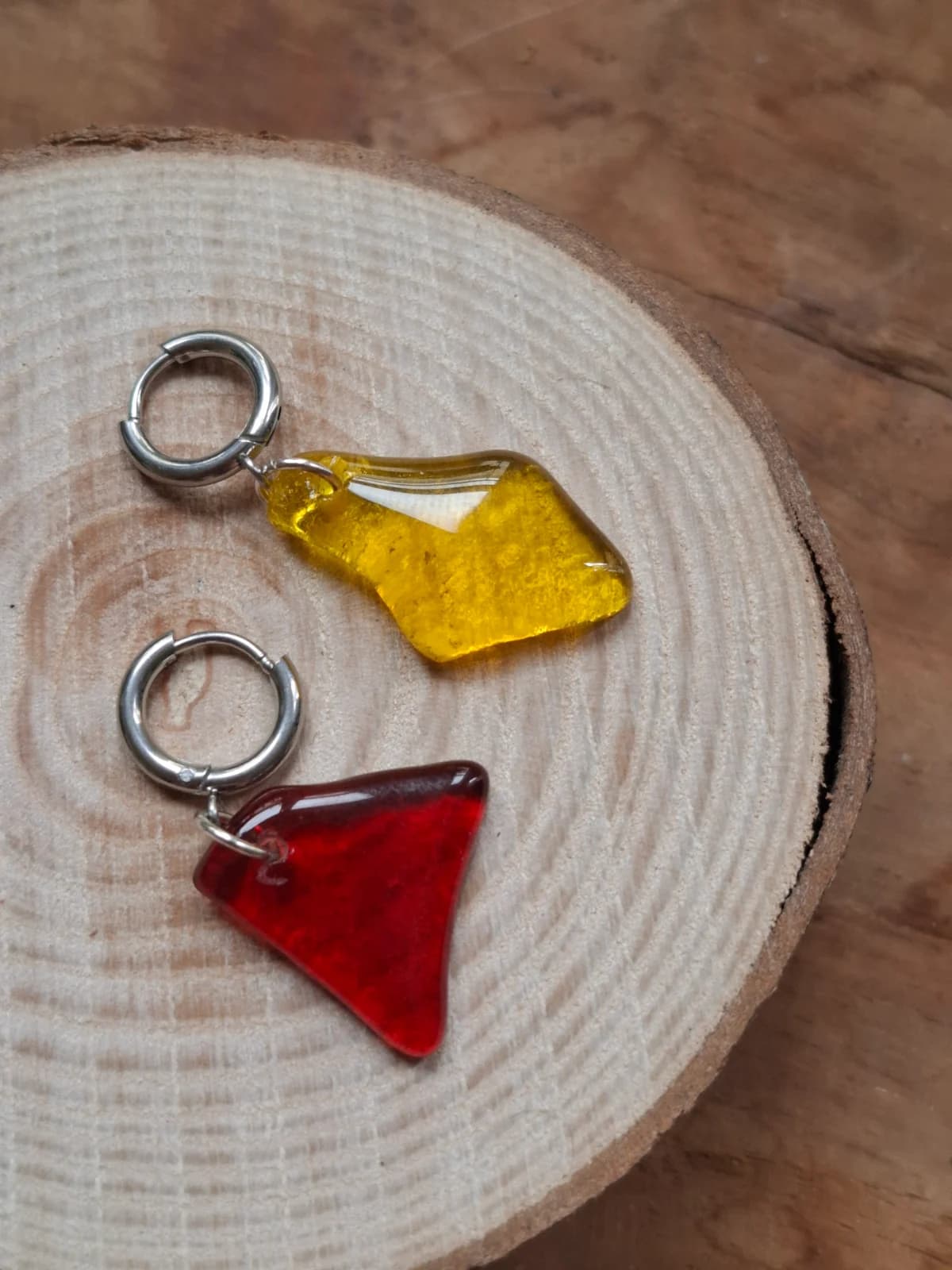 Boucles d'oreilles dormeuses asymétriques en verre jaune et rouge posées sur une tranche de bois.