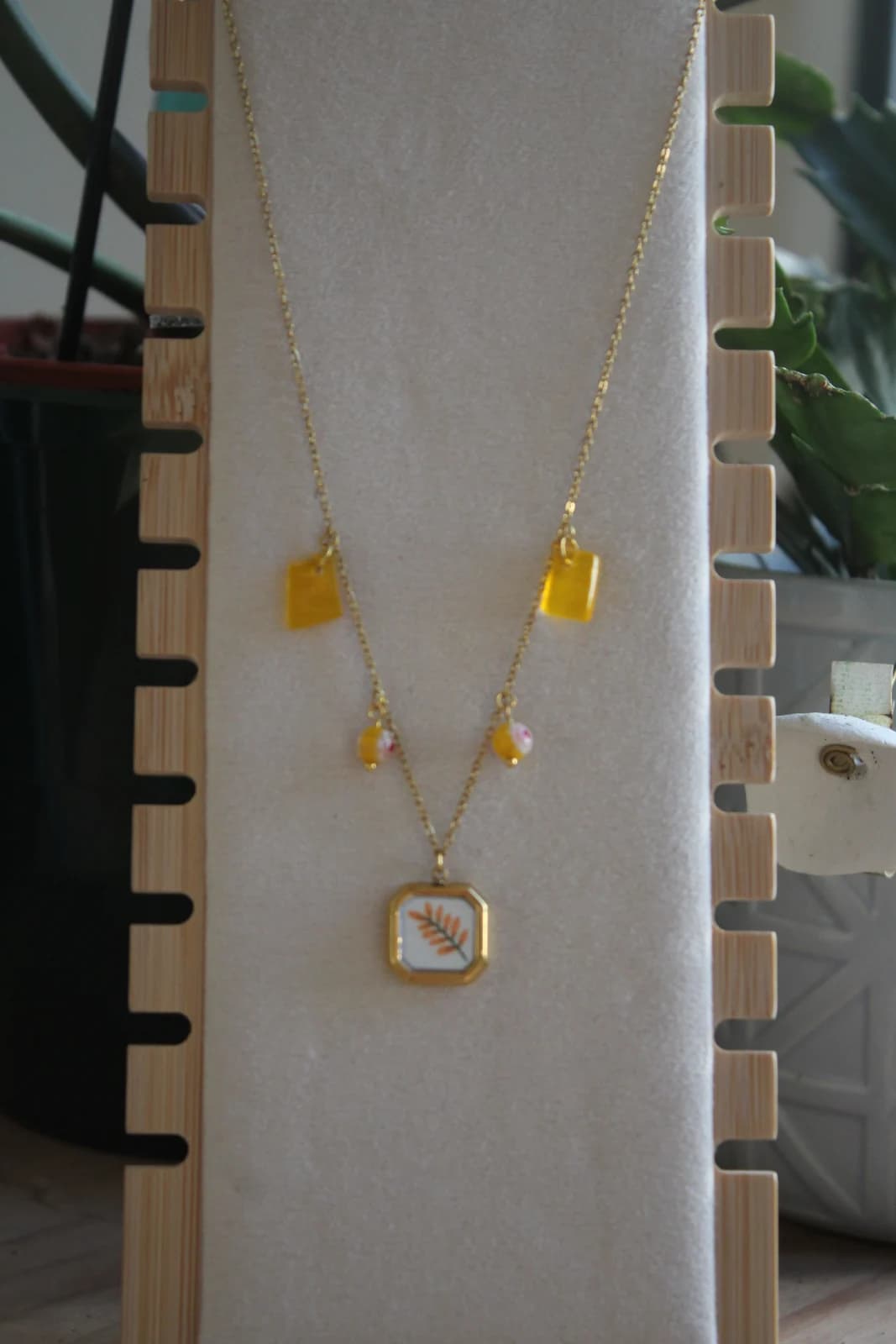 Collier doré à pampilles jaunes et pendentif branche feuillue présenté sur un présentoir vertical.