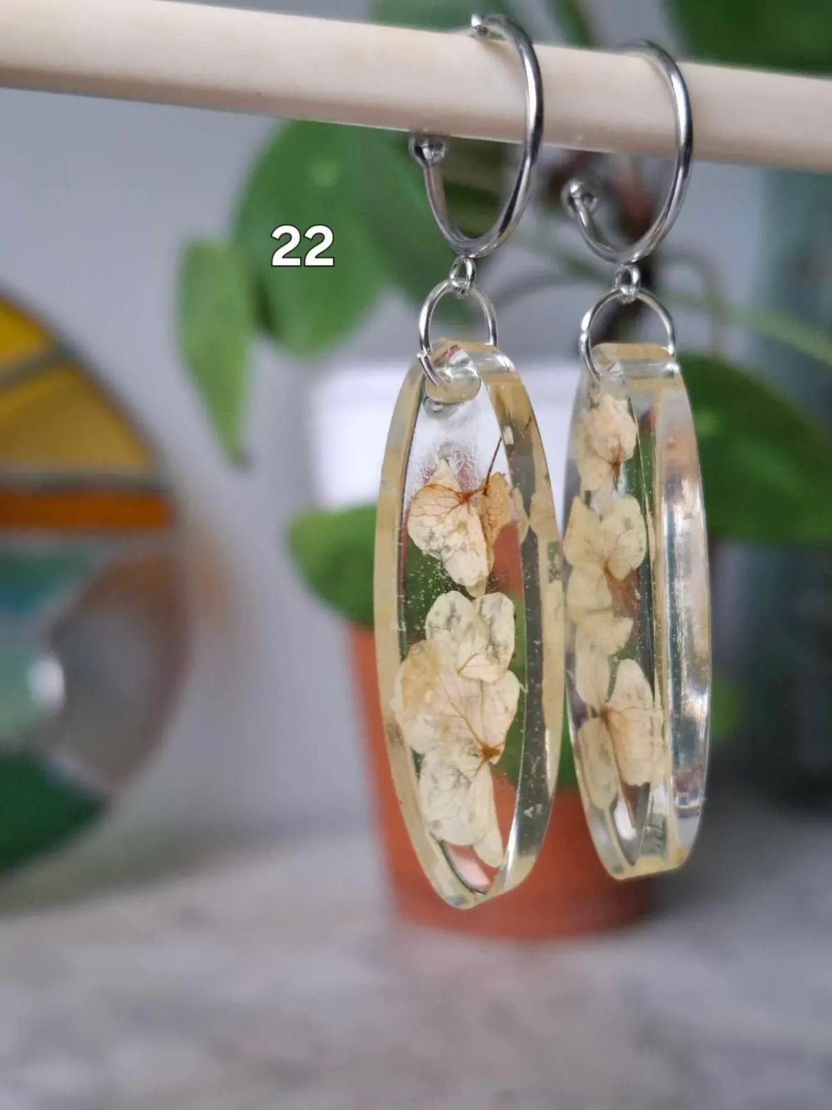 Boucles d'oreilles pendantes ovales en résine transparente avec inclusions de fleurs séchées claires.