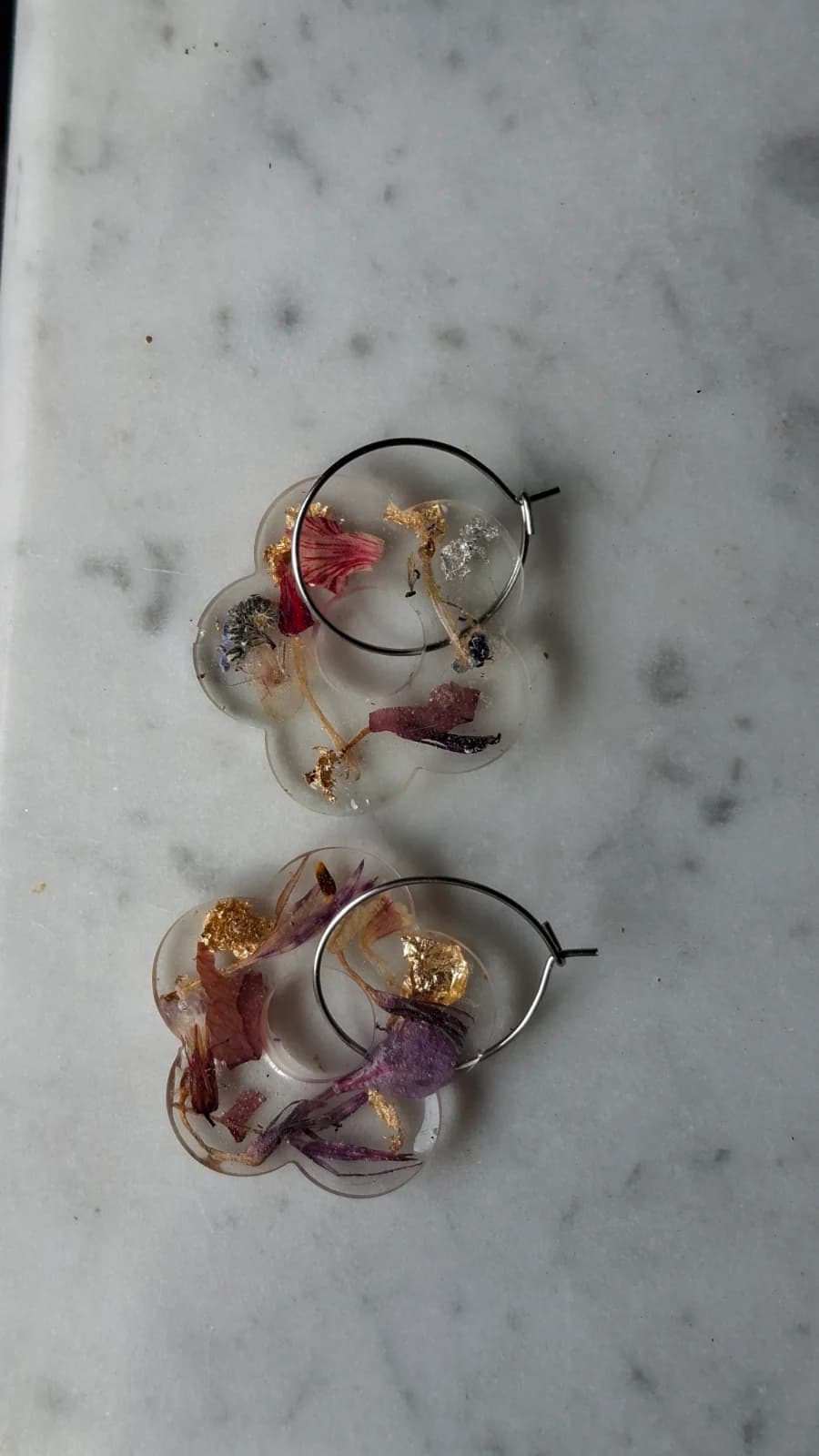 Créoles avec pendentifs en forme de fleur en résine transparente et fleurs séchées posées sur marbre.