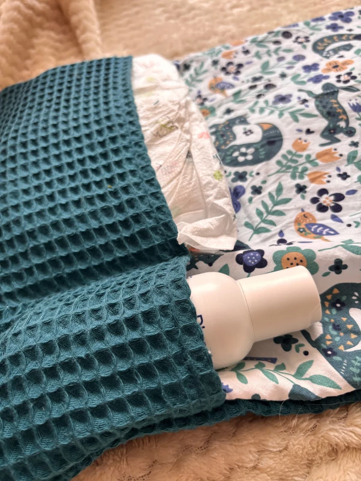 Détail de la poche en nid d'abeille vert foncé du tapis à langer contenant une couche et un flacon blanc.