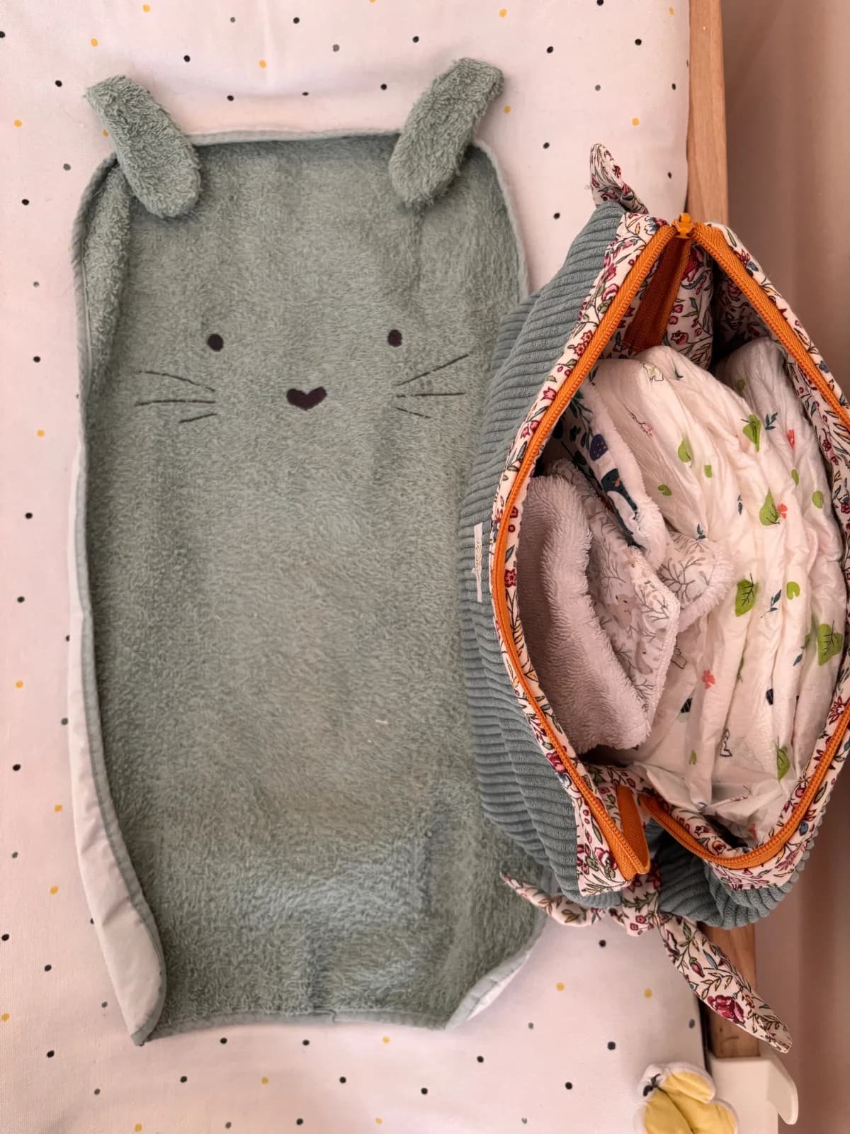 Vue de dessus de la trousse ouverte remplie d'affaires de bébé à côté d'un lange à oreilles de chat.