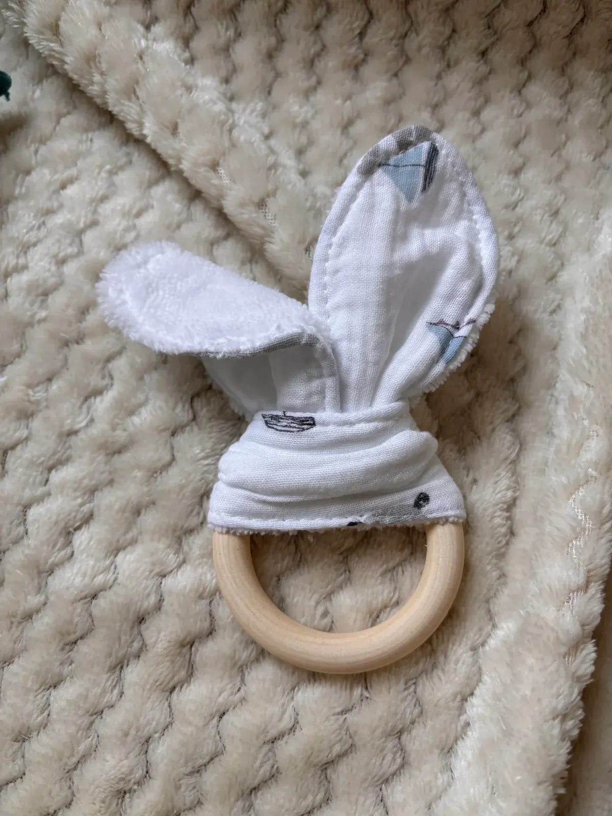 Anneau en bois avec oreilles de lapin en tissu blanc à motifs marins posé à plat sur un plaid écru