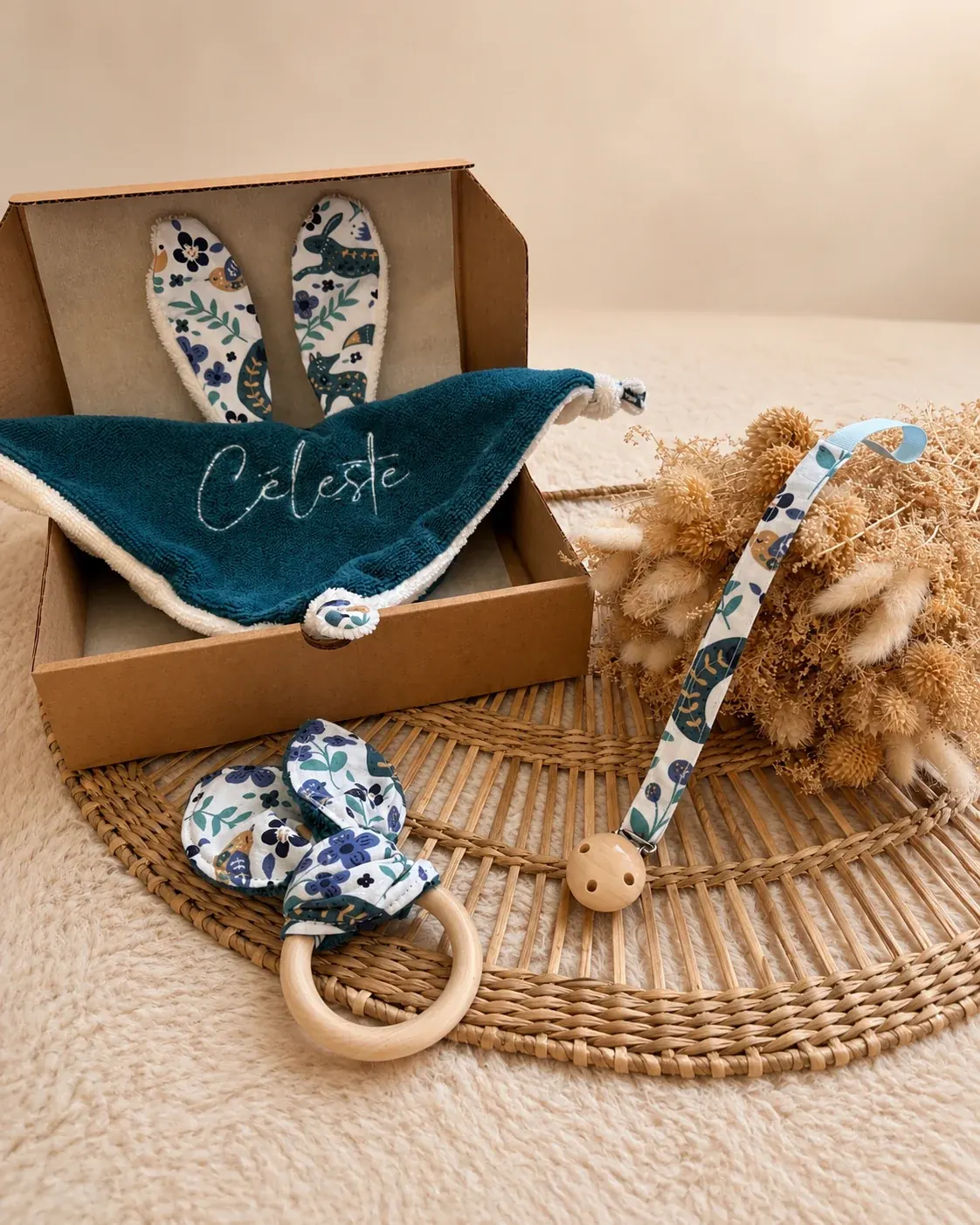 Coffret cadeau en carton kraft ouvert avec doudou bleu brodé Céleste, attache-tétine et anneau de dentition