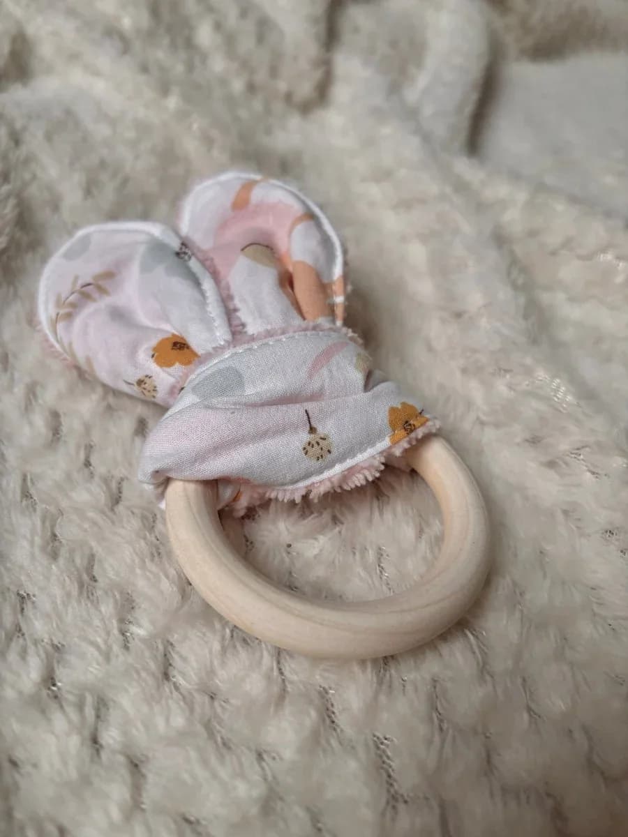 Gros plan sur l'anneau de dentition en bois et ses oreilles de lapin en tissu fleuri.