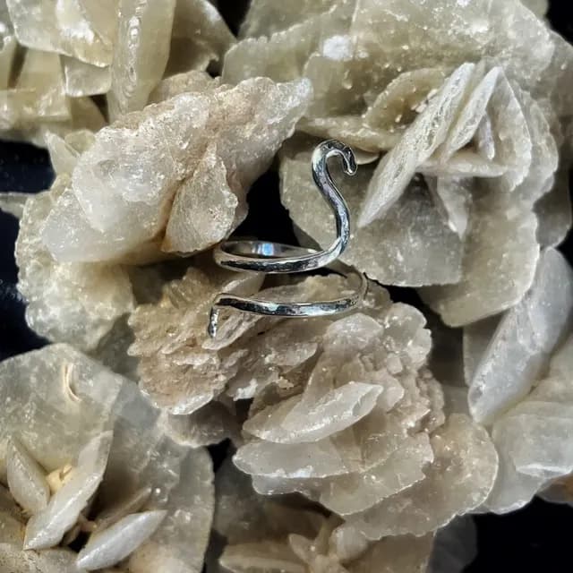 Bague de phalange argentée en spirale posée sur une roche minérale beige.