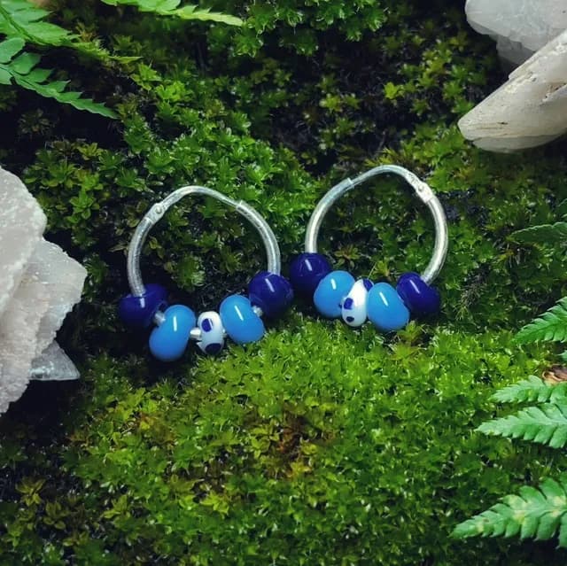 Créoles argentées avec perles de verre bleues et blanches posées sur un lit de mousse verte.
