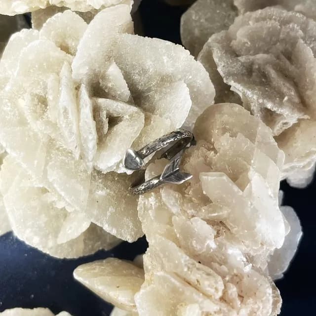 Bague en argent gravé en forme de flèche et cœur posée sur une rose des sables