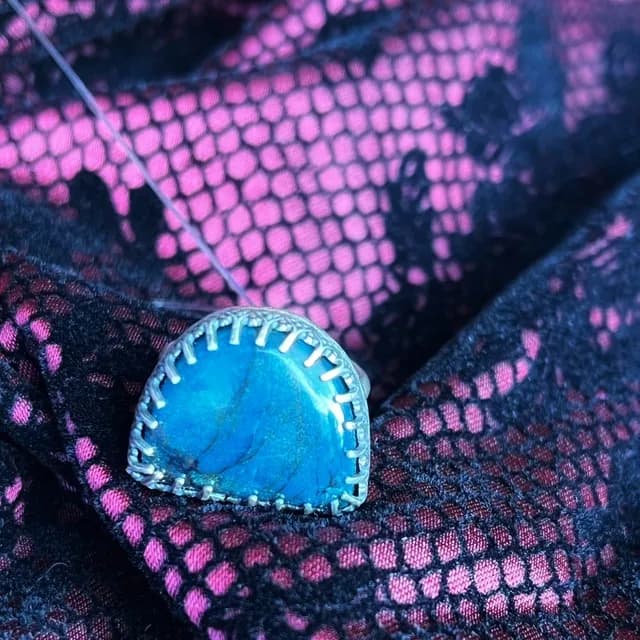 Bague en argent sertie d'une pierre demi-lune bleue sur un tissu texturé rose et noir