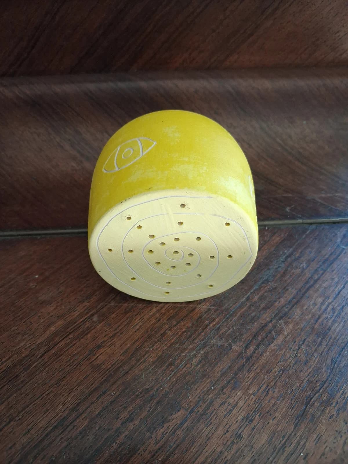 Vue du dessous de la céramique jaune montrant une base plate percée de petits trous en spirale.