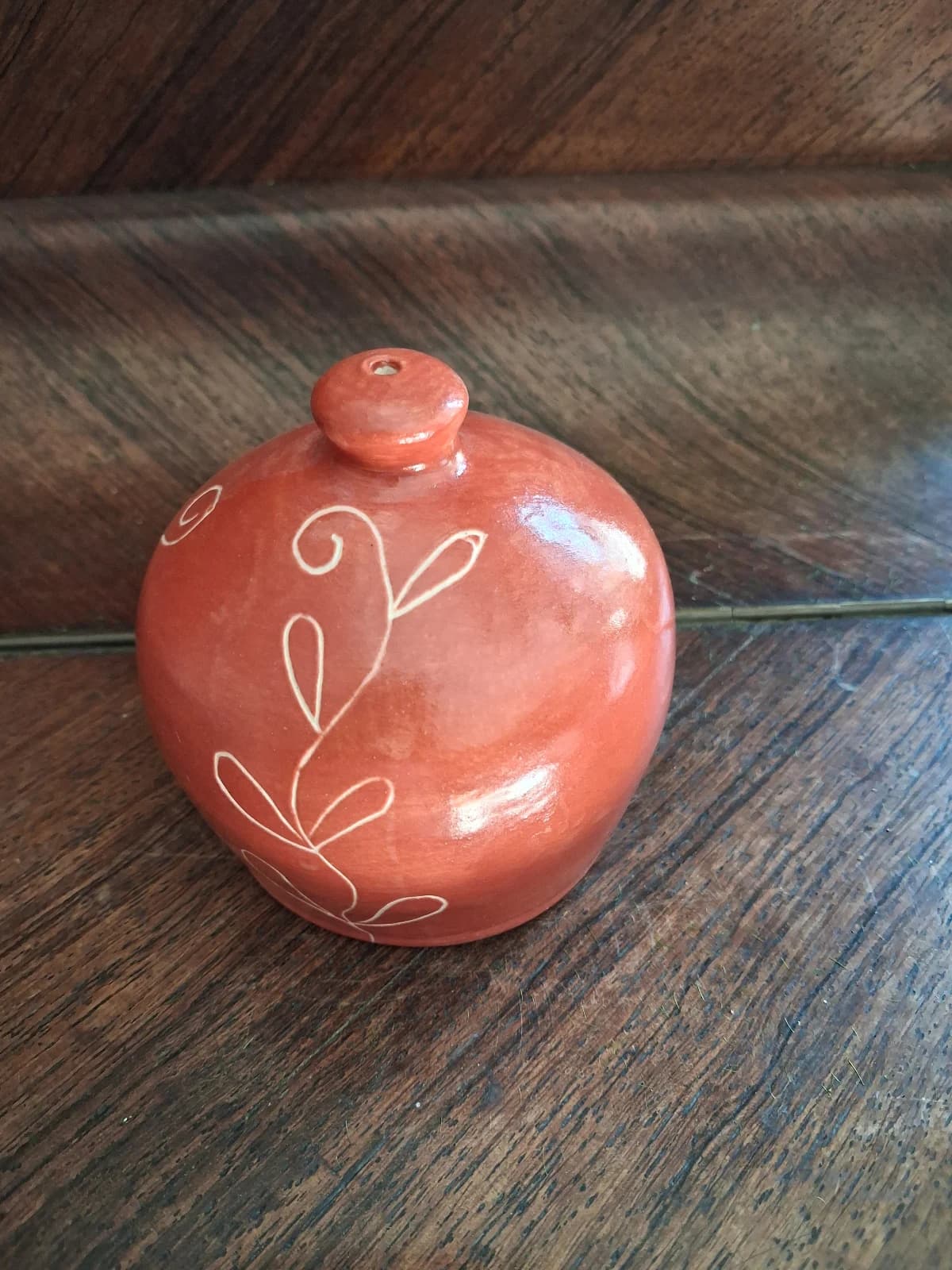 Arrosoir-main rond en céramique rouge brique avec motif végétal blanc sur meuble en bois