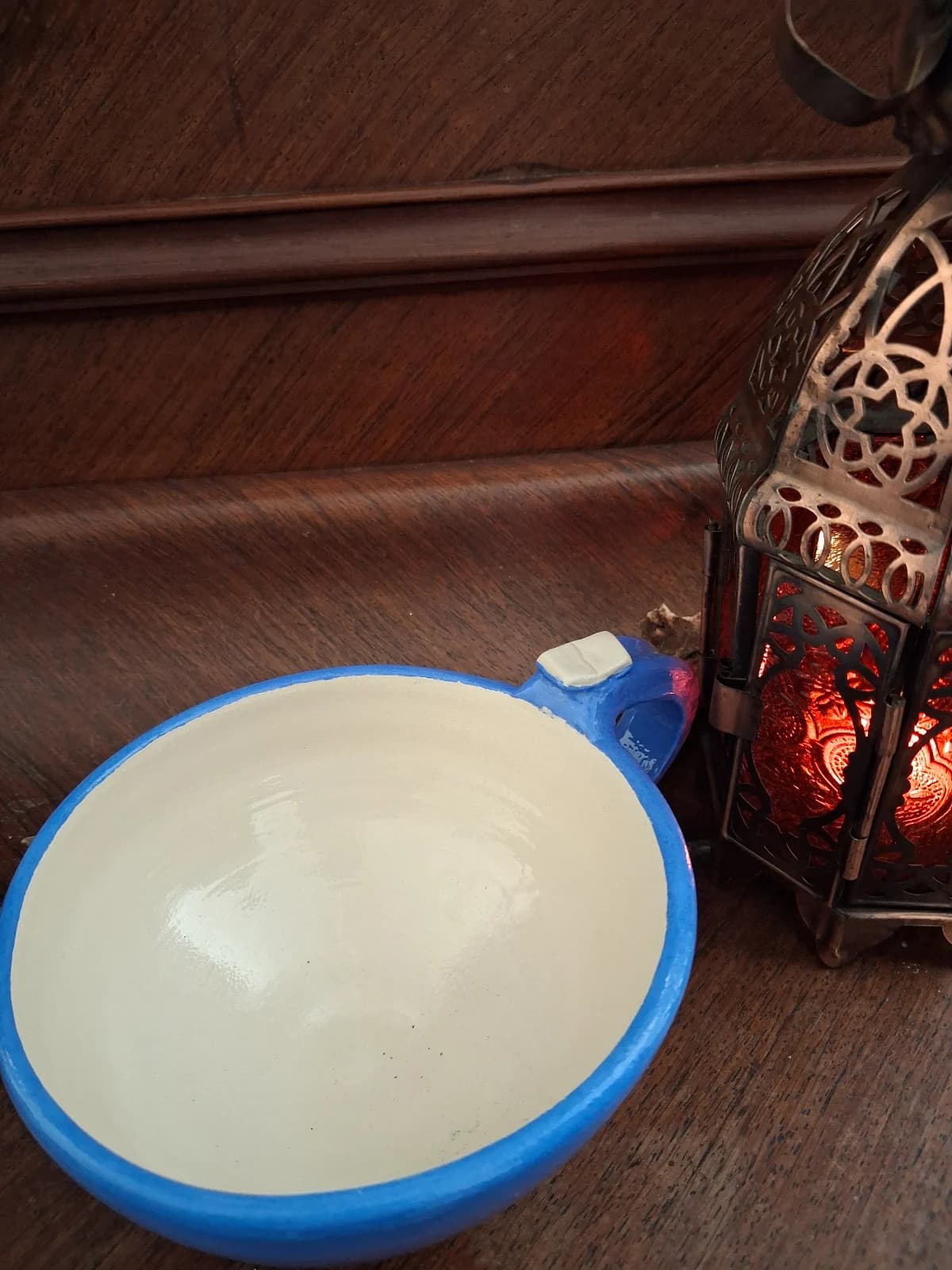 Tasse évasée en céramique bleue et blanche avec détail de livre sur l'anse, posée près d'une lanterne.
