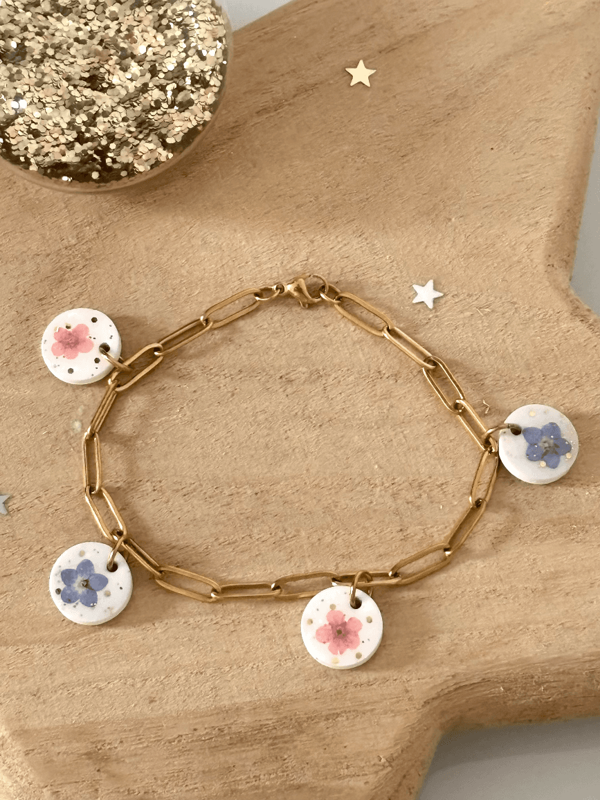 Bracelet chaîne dorée orné de quatre médaillons ronds blancs aux fleurs de myosotis roses et bleues.