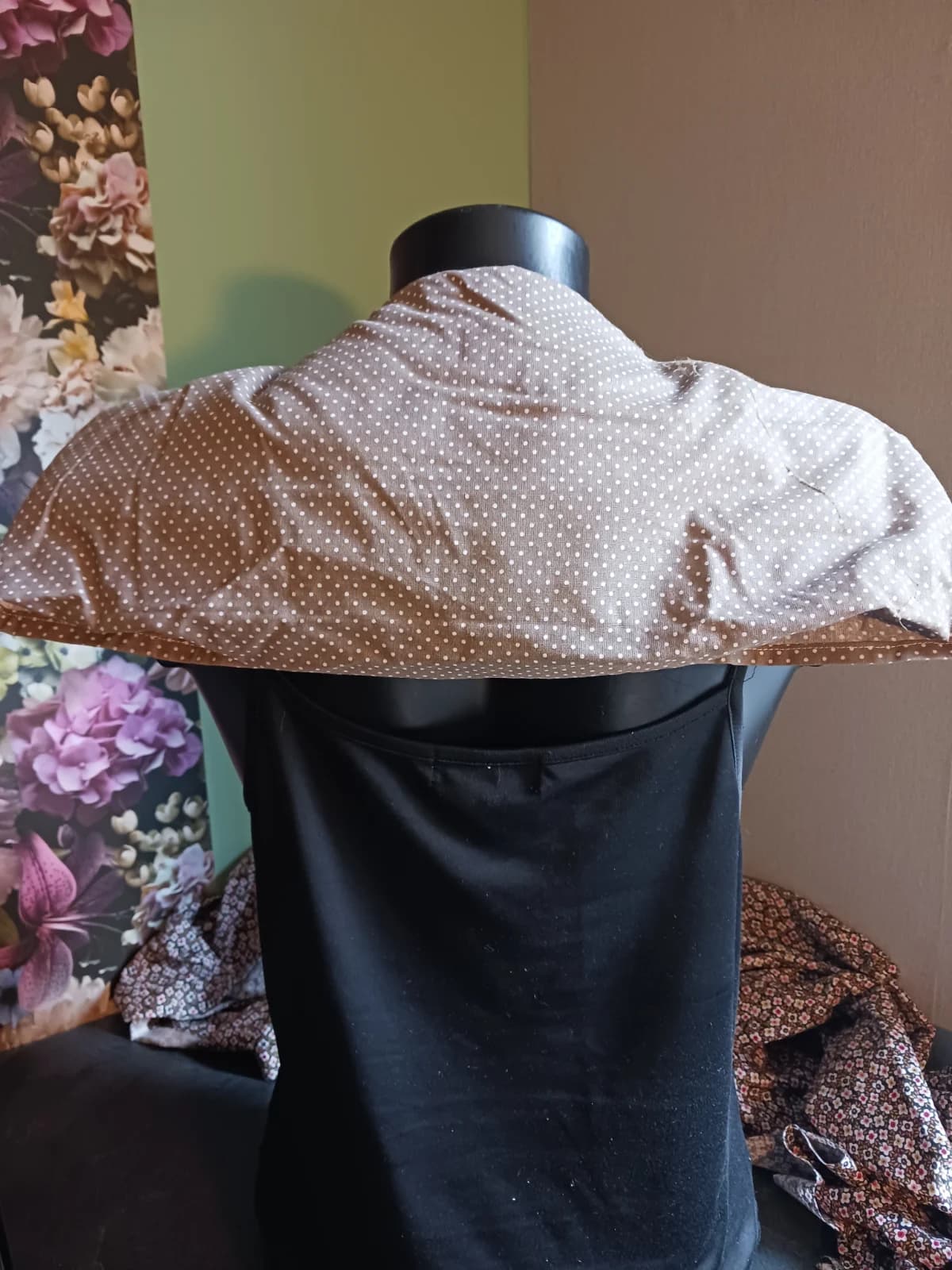 Vue arrière de la bouillotte beige à pois recouvrant la nuque et les épaules d'un mannequin.
