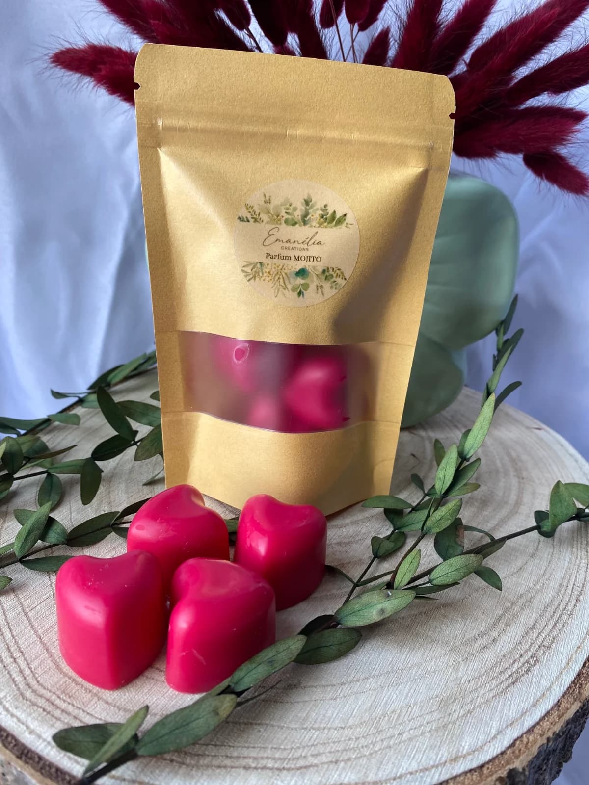 Vue rapprochée de quatre fondants cœurs roses devant un sachet kraft sur une tranche de bois.